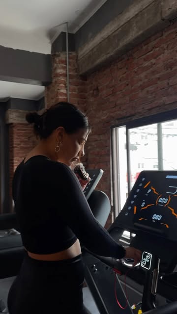 Mujer entrenando en la cinta frente a la pared de ladrillo de Norvik